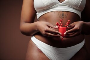 A woman on her period wearing underwear and holding a red menstrual cup