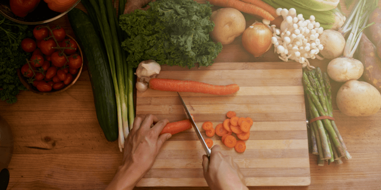 A person's hands preparing a plant-based meal, the chopping board is surrounded by vegetables and other nutrient-rich plant-based ingredients.