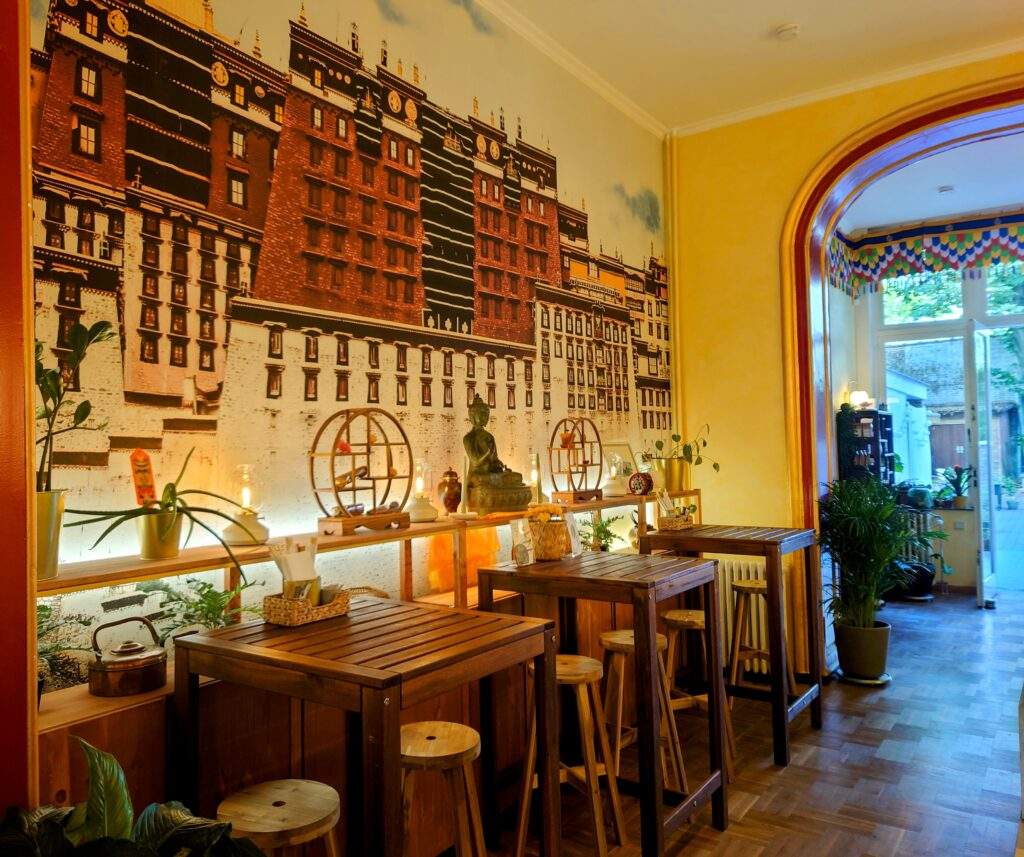 The inside of the vegan Bodja restaurant in Brussels, you can see tables against a yellow wall with tall buildings painted on. There is a Buddha statue on a shelf against the wall.
