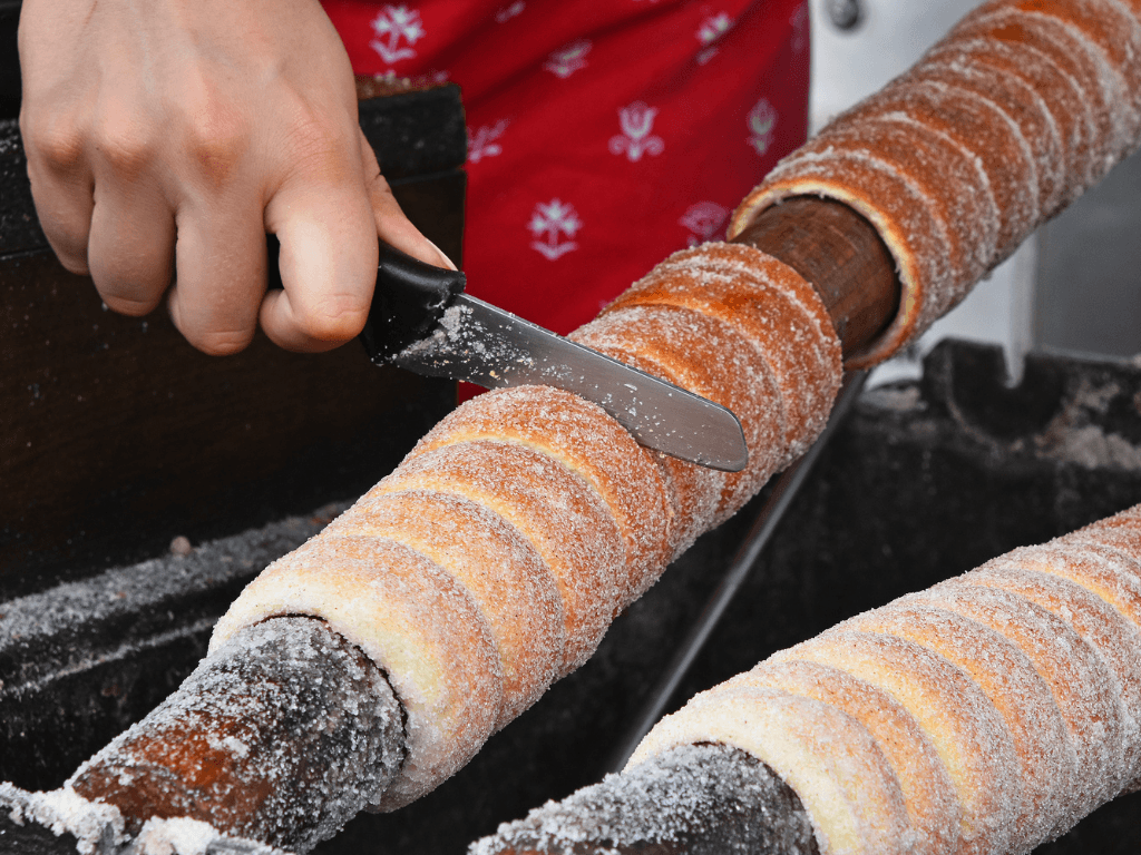 A close up of chimney cake (Kürtöskalács in Hungarian). You can see how deliciously crunchy the dough is on the outside and there is a side view of how light and fluffy the dough is on the inside. The vegan cake is cylindrical and covered in sugar.