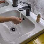 A hand getting wet under a running tap. You can see Inclusev powder-to-lather facewash on the side