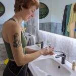 A woman lathers a waterless beauty product in her hands. She's stood by a sink.