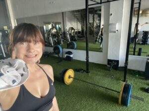 Sweaty vegan Alice taking a selfie in a Mexican gym. There's a deadlift barbell setup in the background.