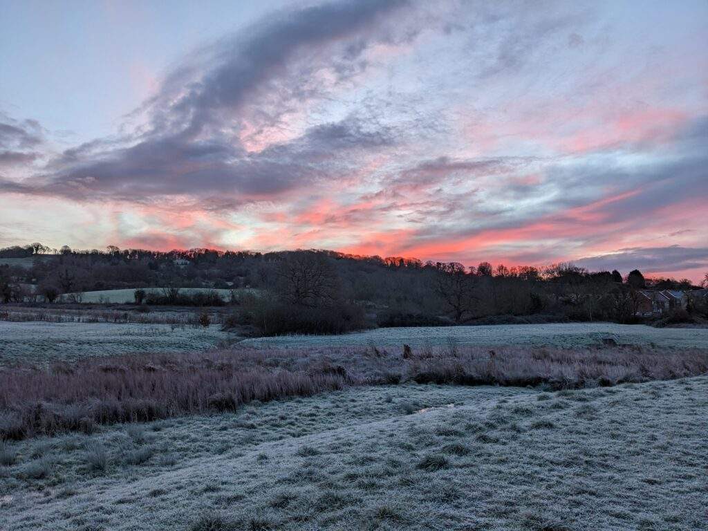 A pink and lilac hued sunrise over frosty fields