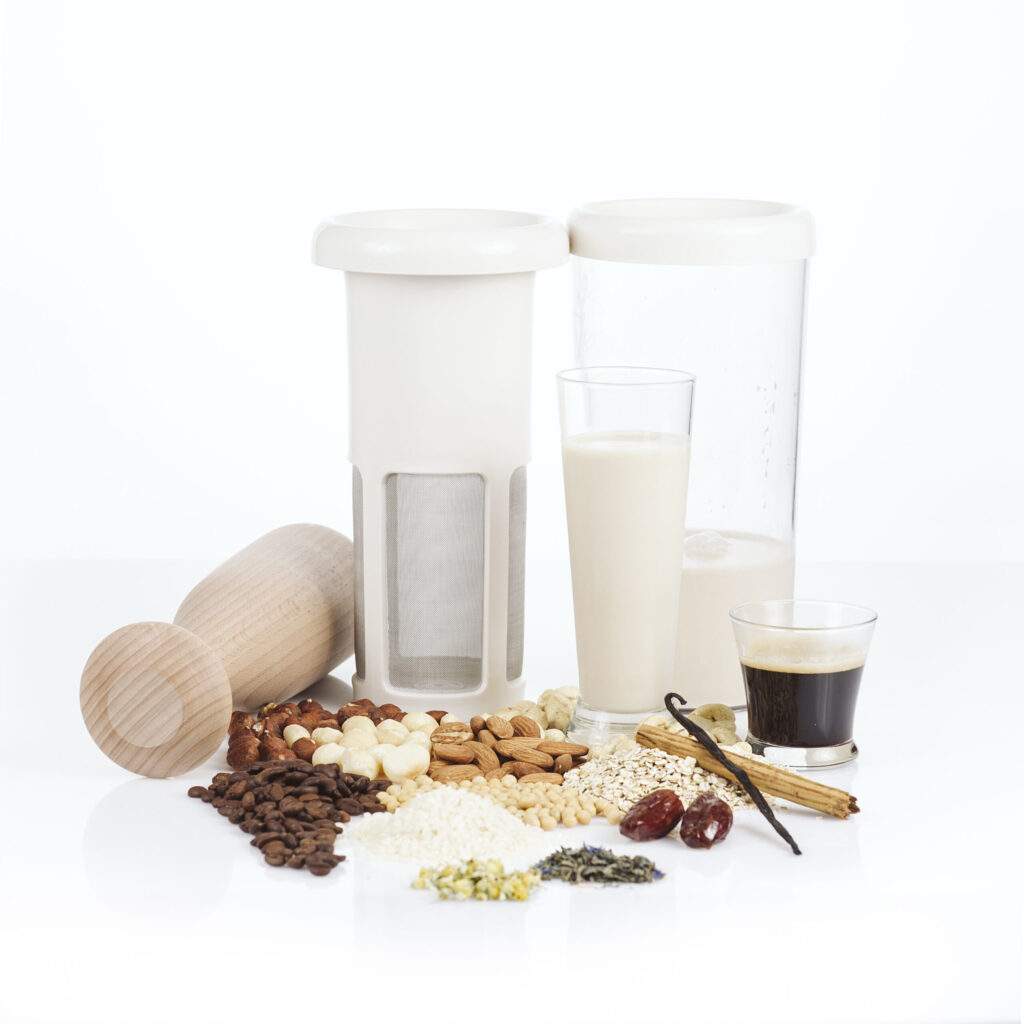 A multifunctional filter strainer in its constituent parts. The container is full of vegan milk and it's surrounded by different types of nuts and flavourings.