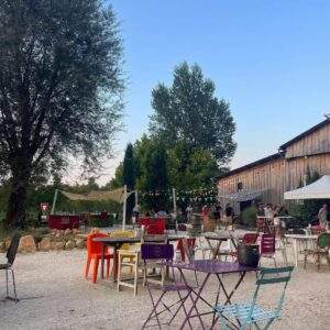 The outside area of Le Trait d'Union in Castelnaud-la-Chapelle, France. There are eclectic garden chairs and tables with fairy lights and a converted barn that houses the vegan-friendly cafe/restaurant