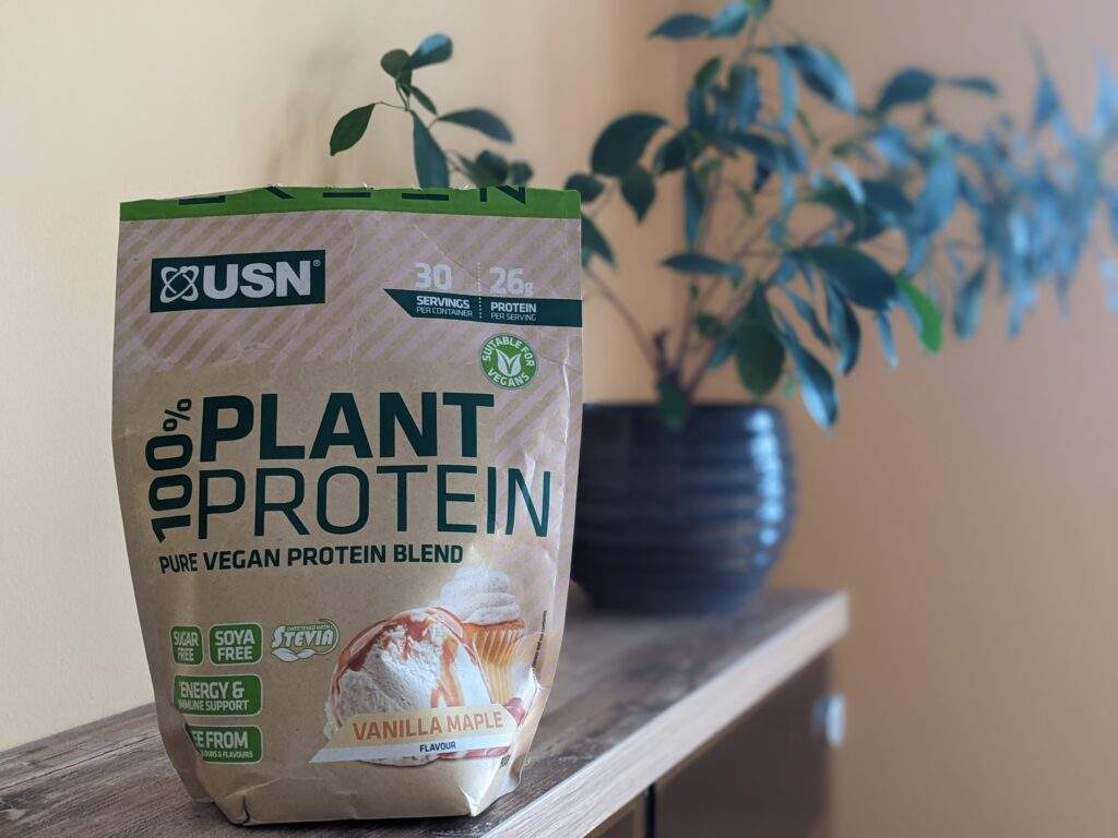 A bag of USN's 100% plant protein in vanilla maple flavour. It's on a cabinet in front of a green leafy plant