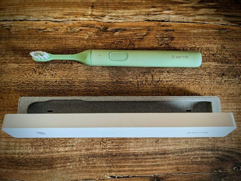 An electric toothbrush is lying adjacent to a travel case on a wooden surface