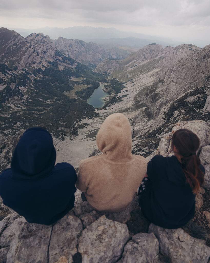 Alice, her friend and her partner are sat on the edge of a mountain overlooking Škrčka jezera (a lake in Durmitor National Park)