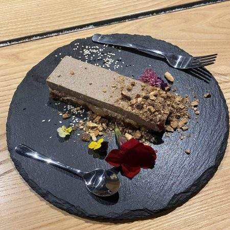 A slice of raw vegan salted caramel and almond dessert on a slate plate and decorated with flowers and crushed pistachios