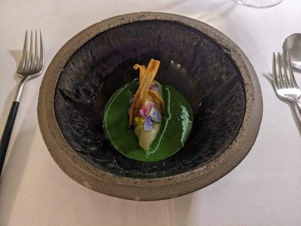 A bowl of parnsip sorbet in a puddle of fresh cress soup with edible flowers and parsnip crisps