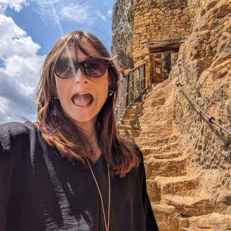 Alice is making a funny face as she takes a selfie halfway up the stairs built into the cliffside at La Roque-Gageac, France